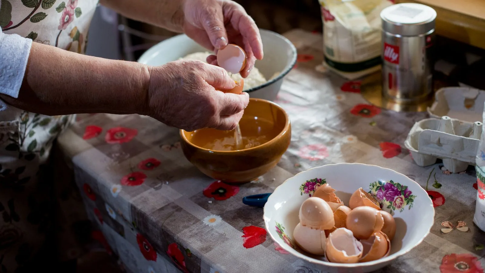 Manos de una persona mayor cascando huevos mientras cocina en su casa