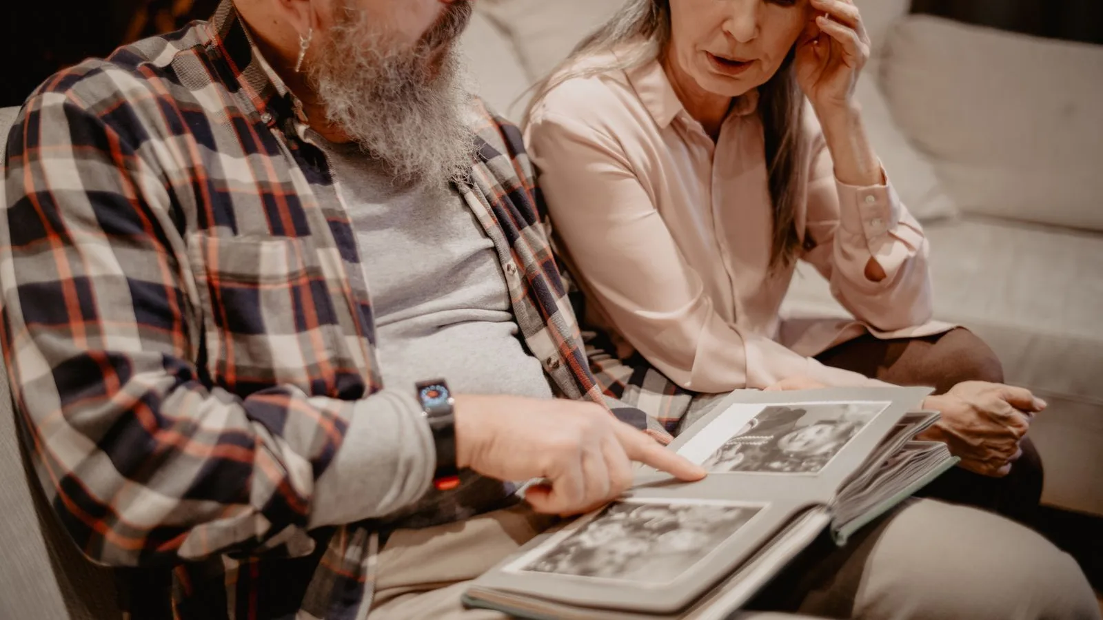 Pareja mayor mirando juntos un álbum de fotos antiguas en el sofá de casa