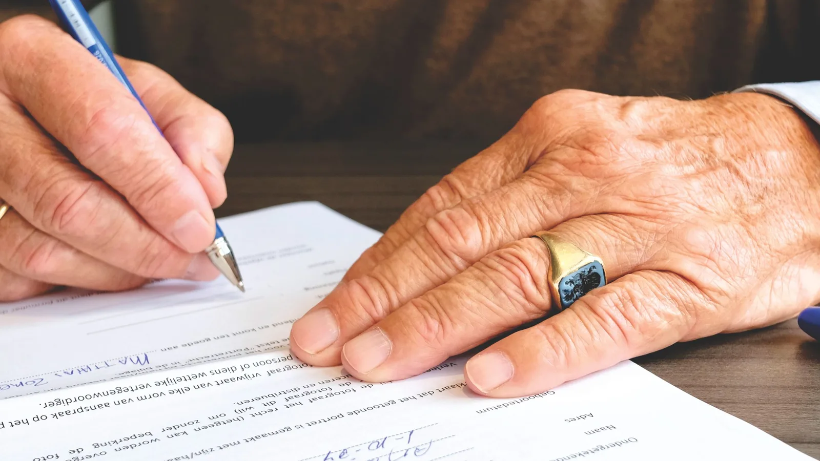 Manos de una persona mayor firmando los papeles de la solicitud de dependencia