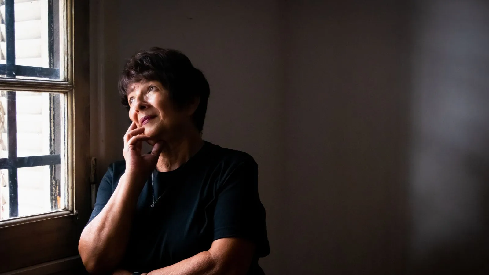 Mujer mayor pensativa junto a la ventana de su casa