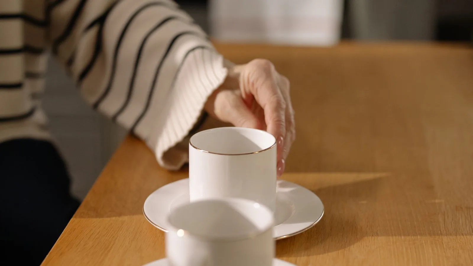 Mano de una persona mayor alcanzando con cuidado una taza sobre la mesa