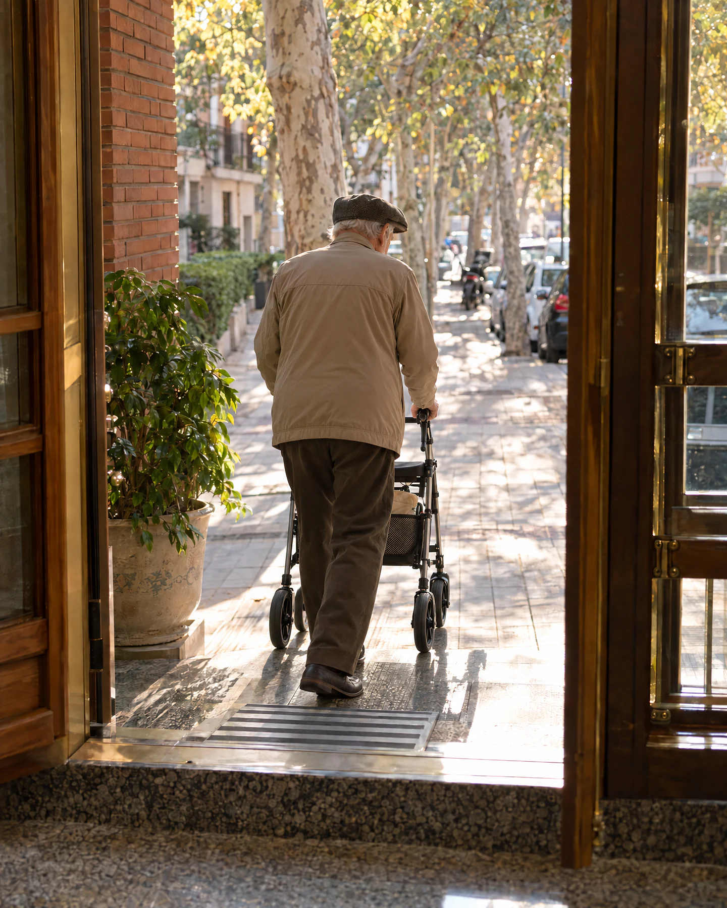Hombre mayor saliendo del portal de su casa a la calle con un andador de cuatro ruedas